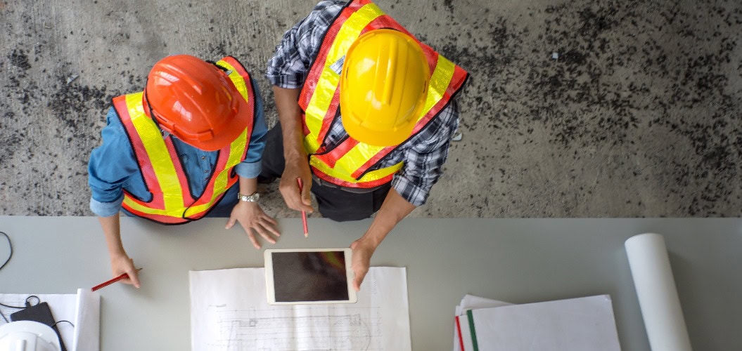 Draufsicht auf eine Gruppe von Ingenieuren, die sich treffen, um Bauarbeiten zu planen, Papierpläne auf der Baustelle ansehen, Draufsicht, Konzept für Teamarbeit